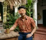 Man in Boriby Ajrakh Printed Half Shirt seated in tropical courtyard with brass cup